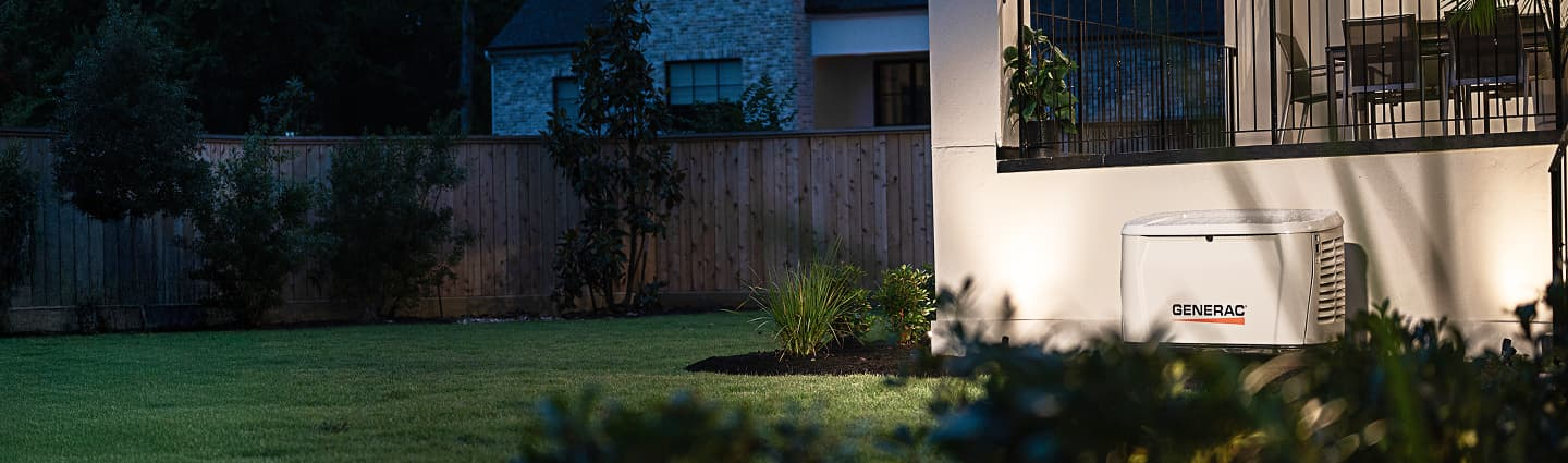 Generac standby generator beside an illuminated home at dusk