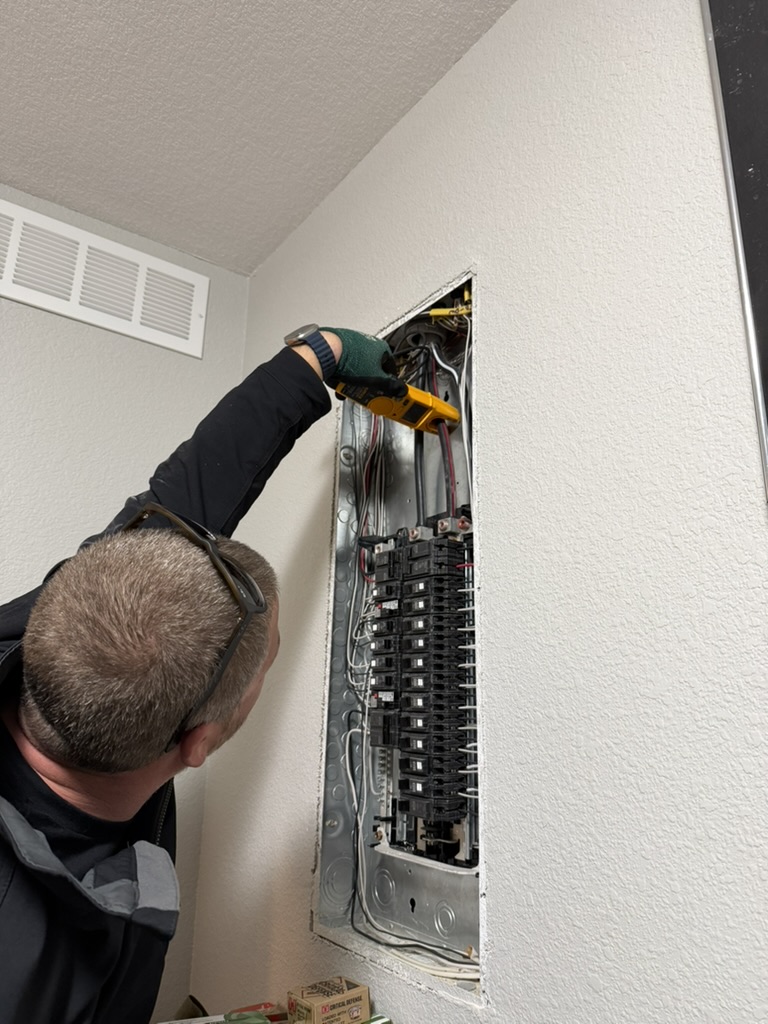 Electrician using a clamp meter at an open electrical panel