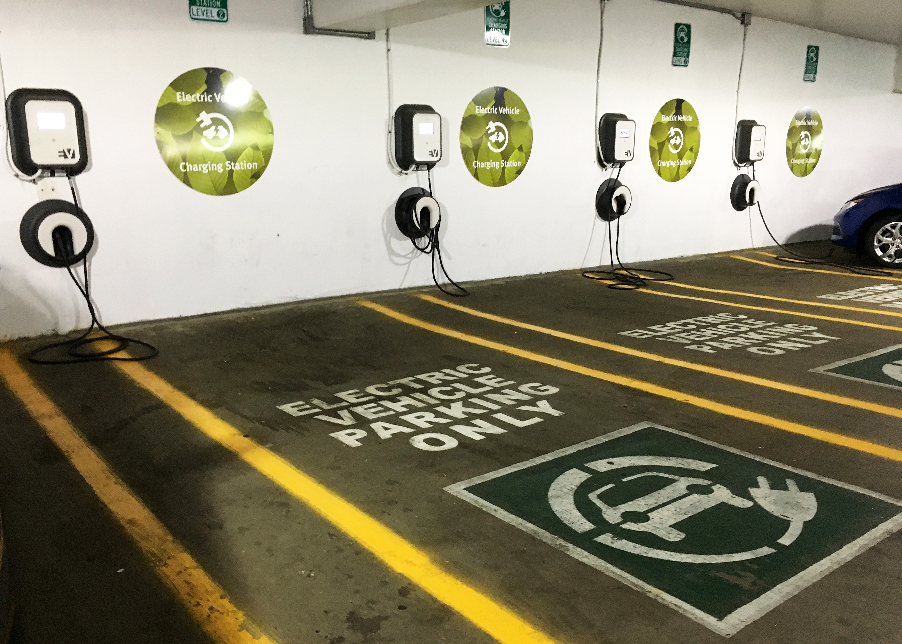 A row of wall-mounted EV chargers beside marked parking spaces in a commercial garage.