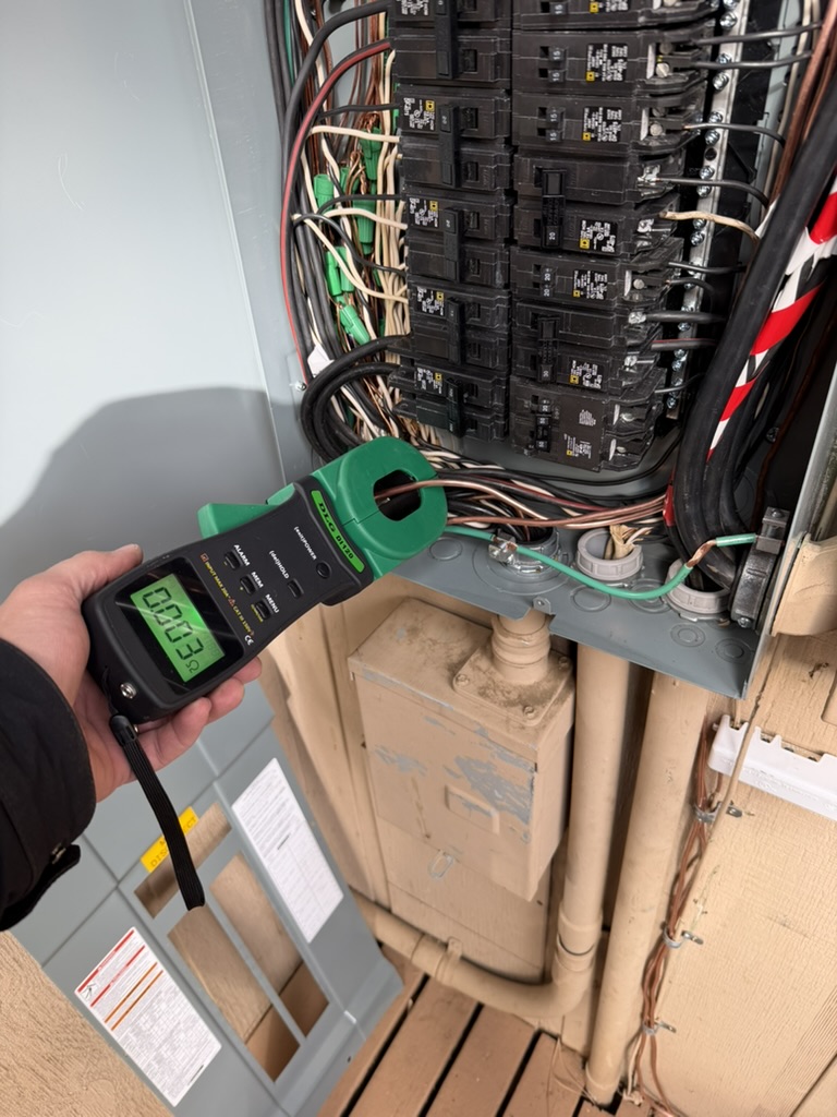 Clamp-style ground resistance tester around a conductor at an open panel