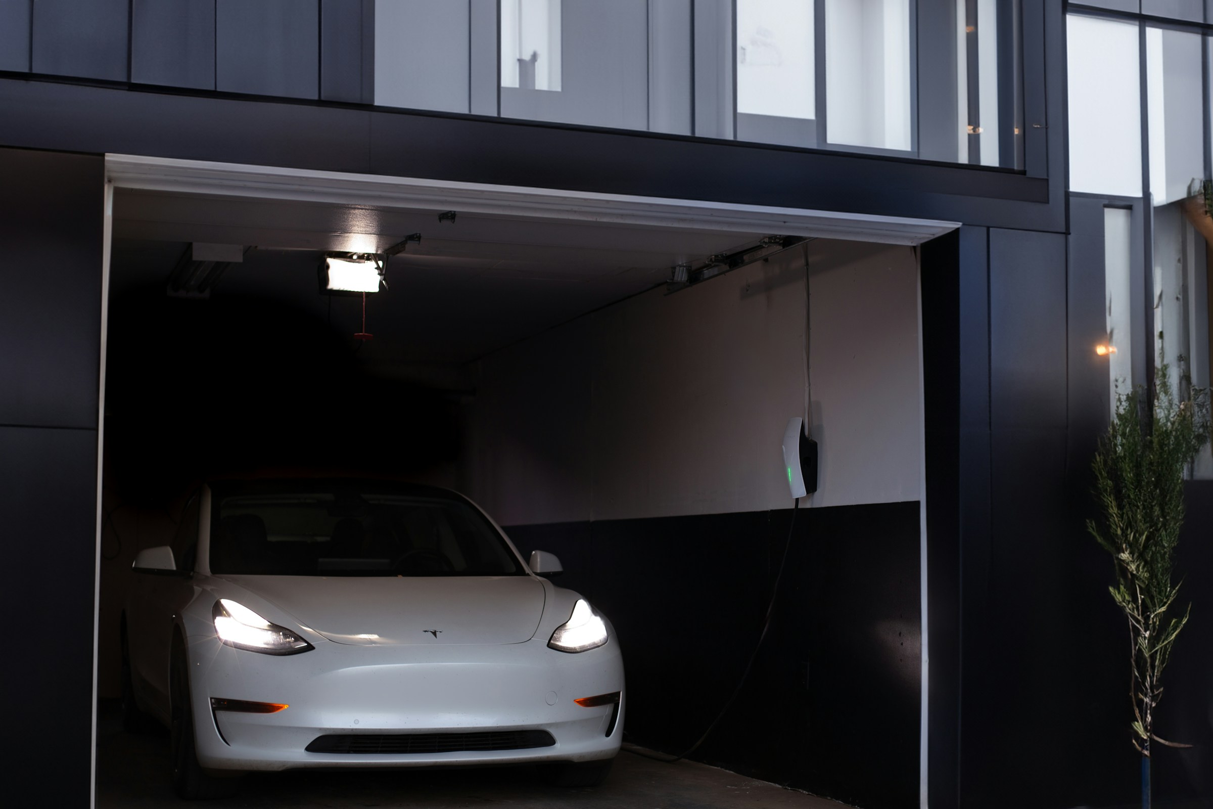 White electric car in a residential garage with a wall-mounted charging unit.