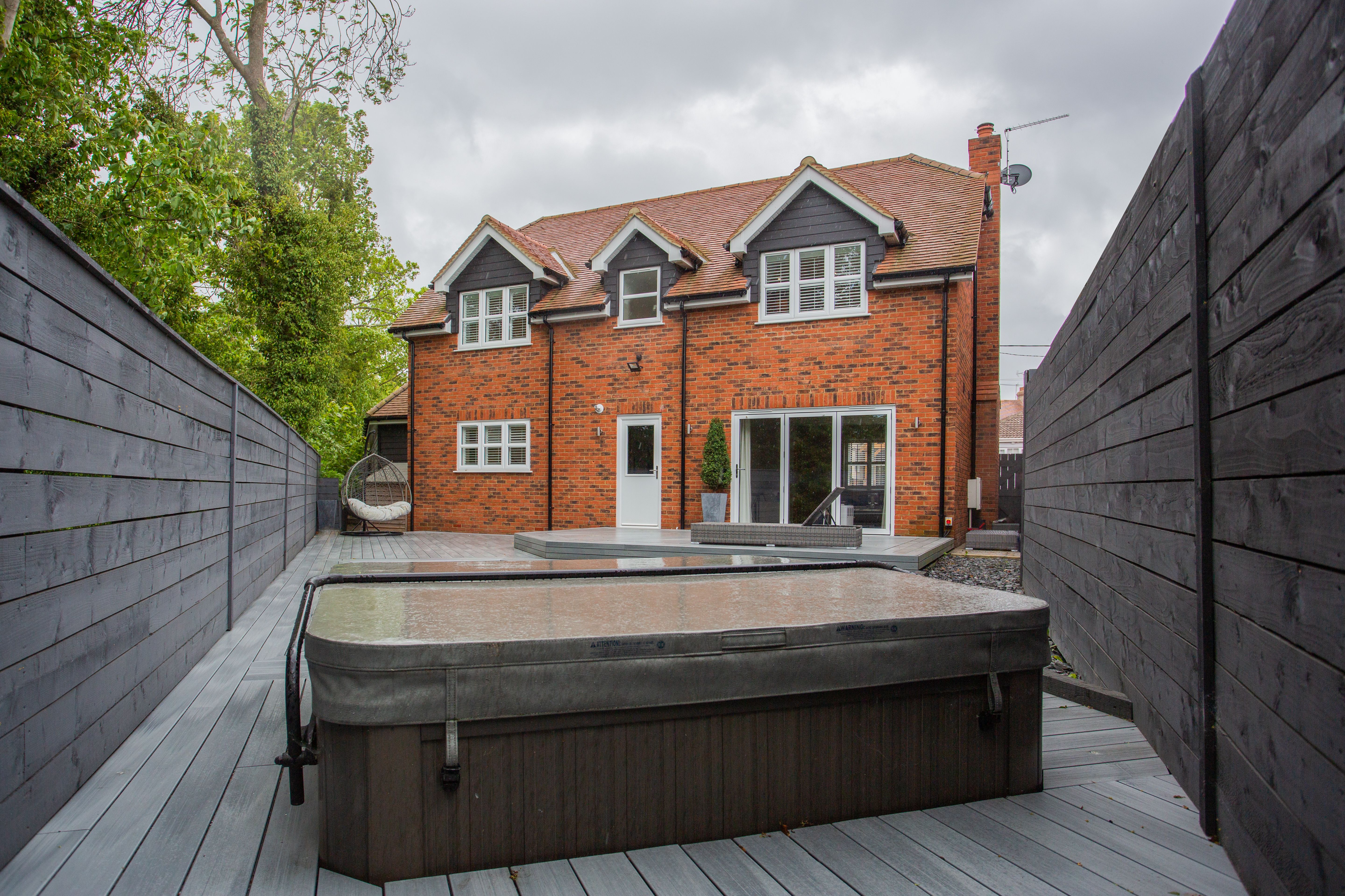 Covered hot tub on a backyard deck beside a brick house.