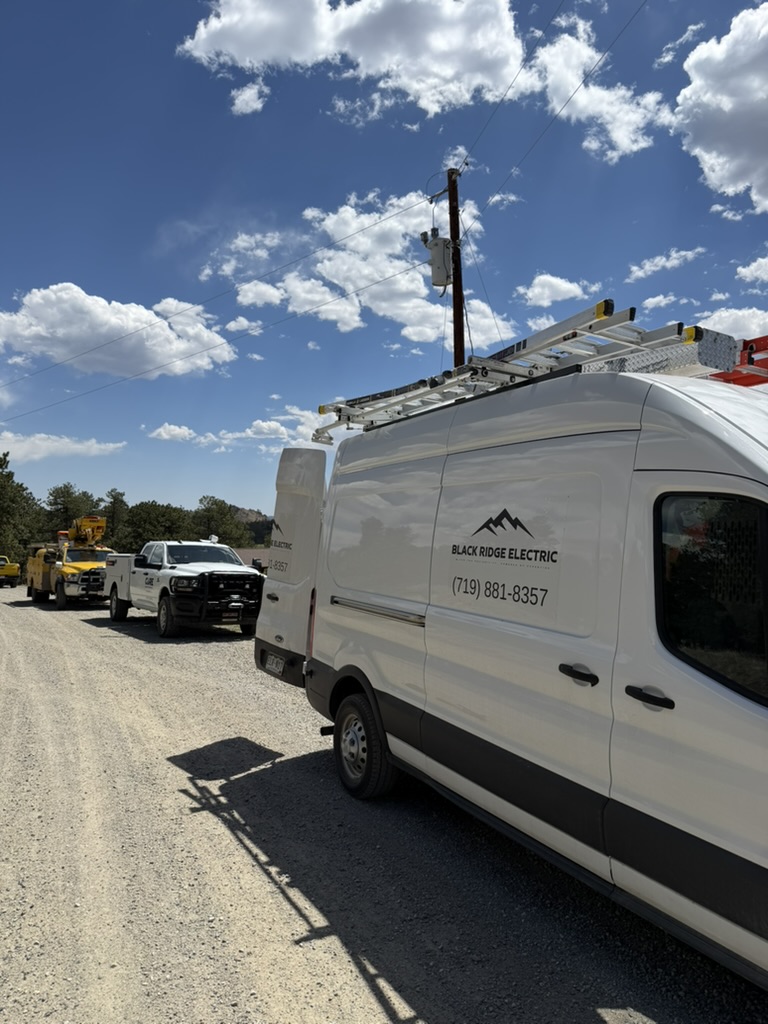 Black Ridge Electric van beside utility trucks working along a road