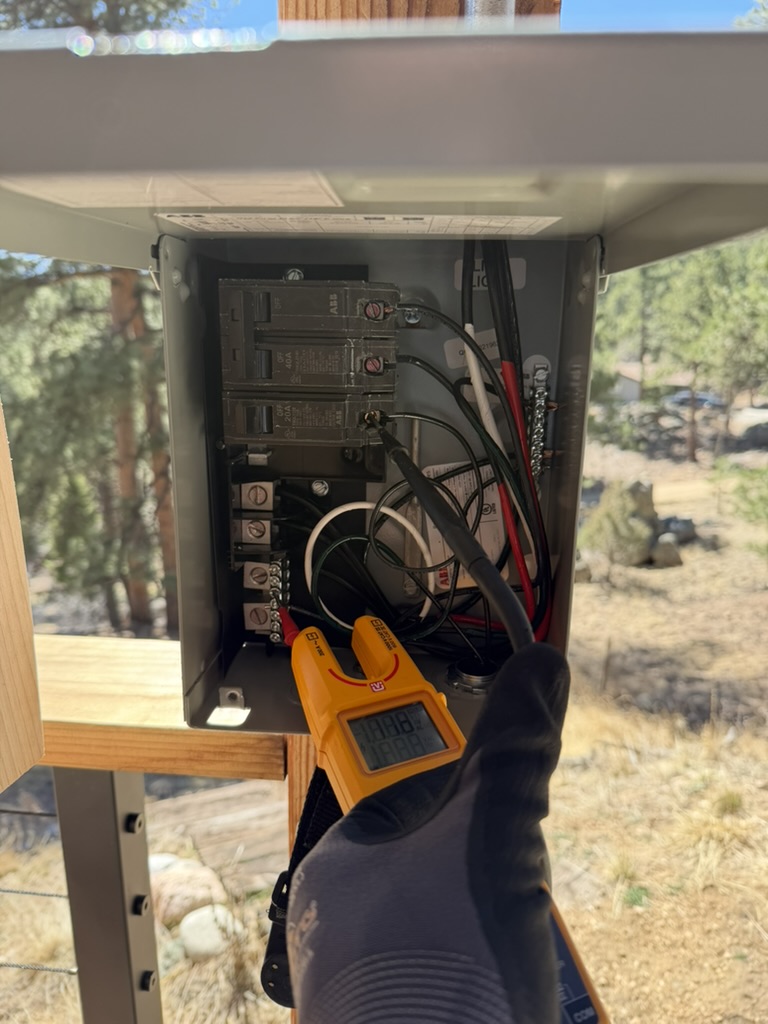 Multimeter measuring voltage at an open outdoor electrical panel